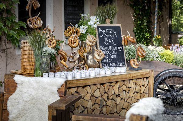 Ein im Freien aufgebauter, festlich dekorierter Holztisch für Feierlichkeiten als Bar zur Auswahl von Brezen und verschiedenen Aufstrichen.