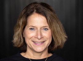 Portrait of a smiling woman with shoulder-length hair against dark backdrop