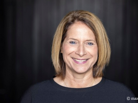 Porträt einer lächelnden Frau mit schulterlangen Haaren vor dunklem Hintergrund