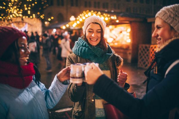 Drei Freundinnen auf dem Adventsmarkt in München stroßen mit Glühwein an.