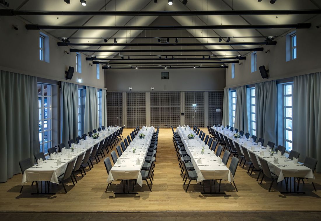 Spacious dining hall with four long, elegantly decorated tables. Each table is adorned with flowers and candles