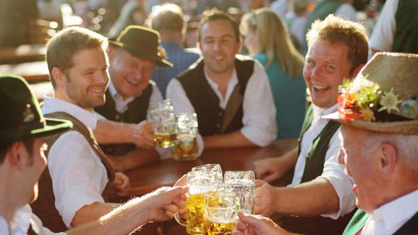 Mehrere Männer in Tracht stoßen mit Maßkrügen im Biergarten an.