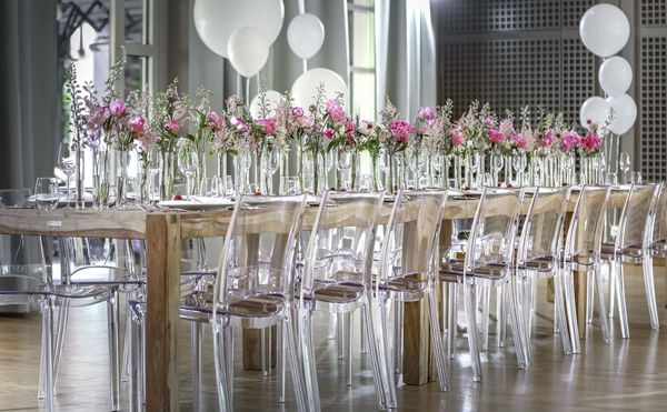 Festliche Tafel mit weiß gedecktem Tisch, rosaroter Blumendekoration und durchsichtigen Stühlen in der Hochzeitslocation Marias Platzl.