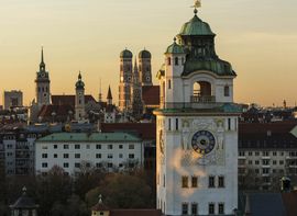 Überblick über die Dächer der Stadt München mit den verschiedenen Kirchtürmen während dem Sonnenuntergang.