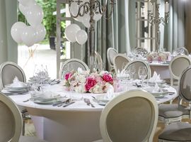 Elegant dekorierter, runder Tisch, eingedeckt mit weißem Gedeck und rosarotem Blumengesteck in der Eventlocation München