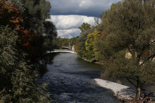 Herbstliche Stimmung an der Isar in München mit Blick auf eine Brücke und von Bäumen gesäumte Ufer.