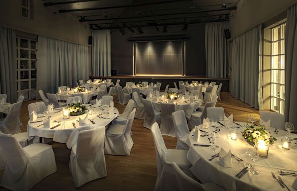 Weiß gedeckte Tische mit Stühlen in weißen Stuhlhussen im Eventsaal in München.
