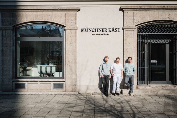 Käsehersteller posieren im Sonnenlicht vor einem Münchner Käsefachgeschäft