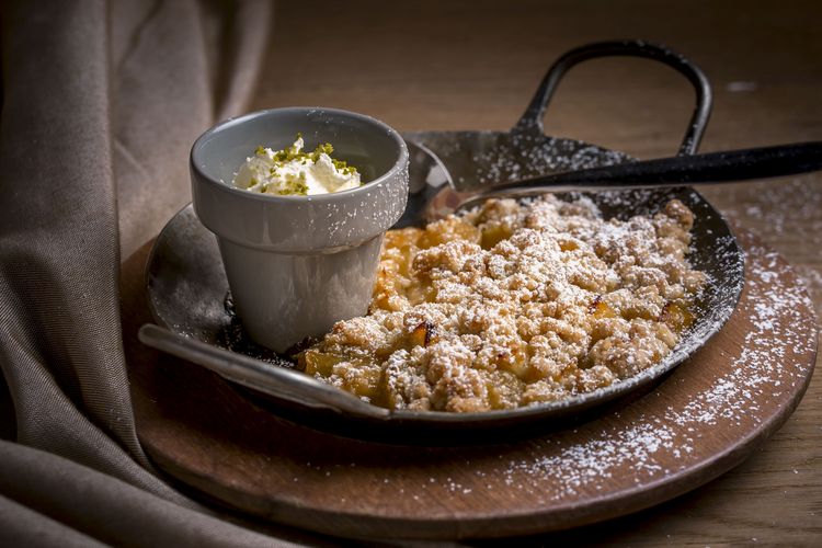 An apple dessert with cream and powdered sugar arranged in a small black pan