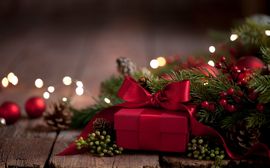 Red-wrapped gift in front of fir branches and Christmas decorations.