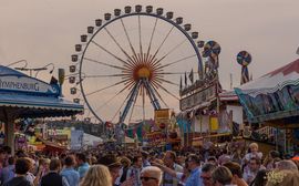 Riesenrad auf dem Oktoberfest in München mit vielen Menschen im Vordergrund bei bewölktem Himmel.
