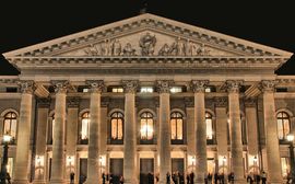 Frontansicht der Münchner Staatsoper bei Abenddämmerung mit vielen Menschen davor