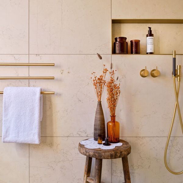 Duschbereich mit Blumenvasen und auf einem Hocker und goldener Duscharmatur.