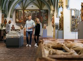 Ein Paar und ein anderer Besucher betrachten die Ausstellungsstücke im Bayerischen Nationalmuseum.