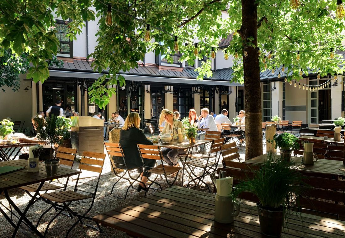 Guests enjoying lunch in a leafy beer garden with wooden tables and hanging lights in the shade