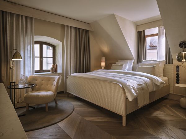 Cozy hotel room with a double bed, an armchair, and wooden flooring under a sloping ceiling.