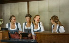 Vier gut gelaunte junge Damen im traditionellen Dirndl an der Rezeption des Platzl Hotels.