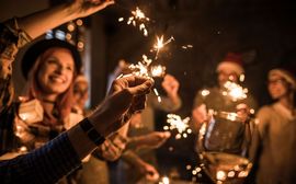 Several people at a New Year's Eve celebration hold up burning sparklers and champagne glasses.