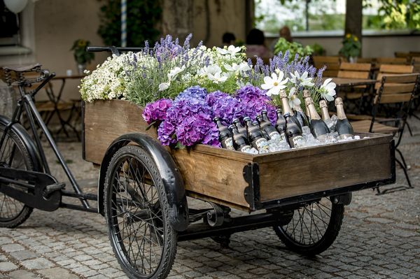Schwarzes Fahrrad mit großem hölzernen Korb, in welchem Blumen, Bier- und Sektflaschen transportiert oder präsentiert werden