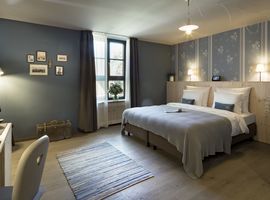 Doppelzimmer Hermine im Boutique Hotel München mit Doppelbett und blauer Tagesdeck, sowie blauer Tapete mit weißen Blumen