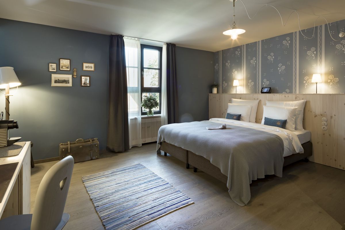 Doppelzimmer Hermine im Boutique Hotel München mit Doppelbett und blauer Tagesdeck, sowie blauer Tapete mit weißen Blumen
