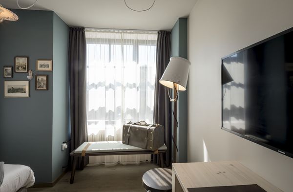 Doppelzimmer Gundi mit Stehlampe und Bank mit Koffer vor dem Fenster im Boutique Hotel München 