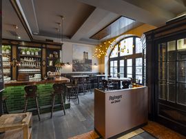 A cozy bar with wooden tables and chairs, and a decorative bottle rack behind the counter.