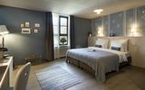 Doppelzimmer Hermine im Boutique Hotel München mit Doppelbett und blauer Tagesdeck, sowie blauer Tapete mit weißen Blumen