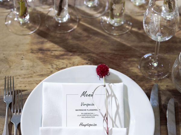 Ansicht von oben auf einen Teller mit einer Menükarte; vor dem Teller viele Blumen in dünnen Vasen in der Eventlocation München