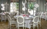 Dining area with white tables elegantly decorated with lit candles, white balloons, and fresh flowers, creating a festive and inviting atmosphere