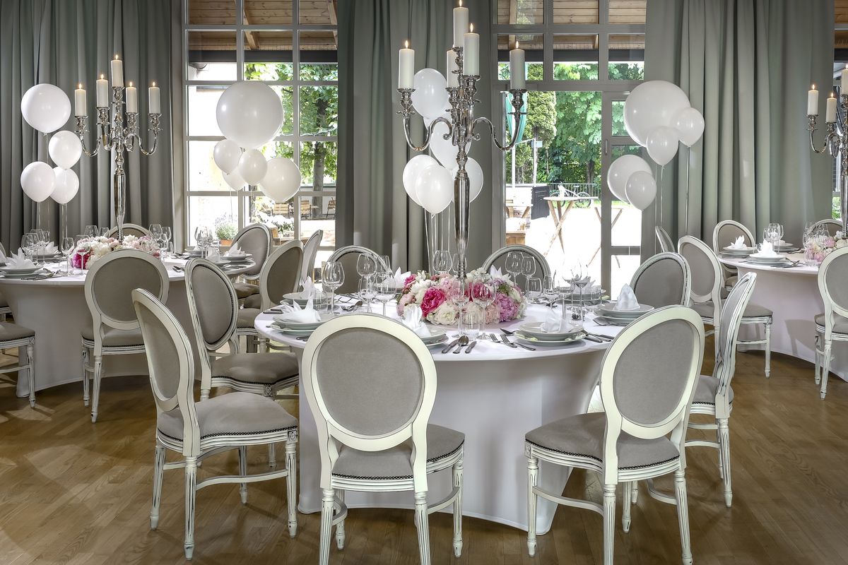 Dining area with white tables elegantly decorated with lit candles, white balloons, and fresh flowers, creating a festive and inviting atmosphere
