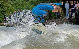 Surfer auf der Eisbachwelle Ein Surfer in blauem Neoprenanzug an der Eisbachwelle vor Zuschauern.