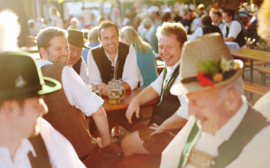 Visitors, dressed in traditional Bavarian attire, are chatting in Ayinger Bräustüberl's beer garden.