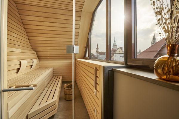 Sauna with wood paneling and benches, large window with a view over the rooftops of Munich's old town.